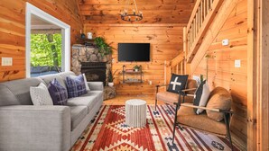 Interior acogedor de una cabaña con detalles de madera, una chimenea, un televisor y un sofá.