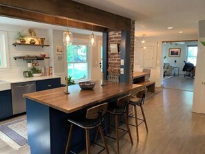 Une cuisine moderne dotée d’un îlot central, de tabourets de bar et de luminaires suspendus.