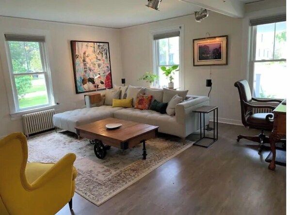 A living room with a sectional sofa, a yellow armchair, a coffee table, and a painting on the wall.