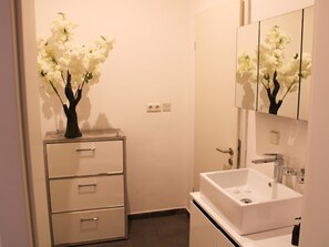 A bathroom with a white sink, a mirror, and a vase with white flowers on a cabinet. - Impeccable 3-bed House in Prampram Accra (Prampram)
