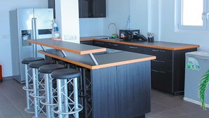 A modern kitchen with a central island, bar stools, a refrigerator, and a microwave. - Impeccable 3-bed House in Prampram Accra (Prampram)