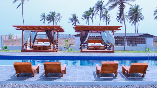 A poolside area with wooden loungers and two wooden beds with canopies. - Impeccable 3-bed House in Prampram Accra (Prampram)