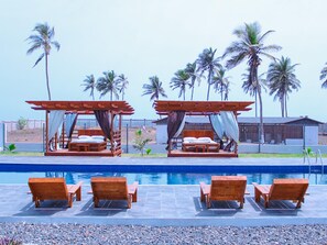 A poolside area with wooden loungers and two wooden beds with canopies. - Impeccable 3-bed House in Prampram Accra (Prampram)