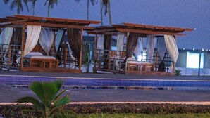 A poolside area with two wooden cabanas, each with a bed and curtains. - Impeccable 3-bed House in Prampram Accra (Prampram)