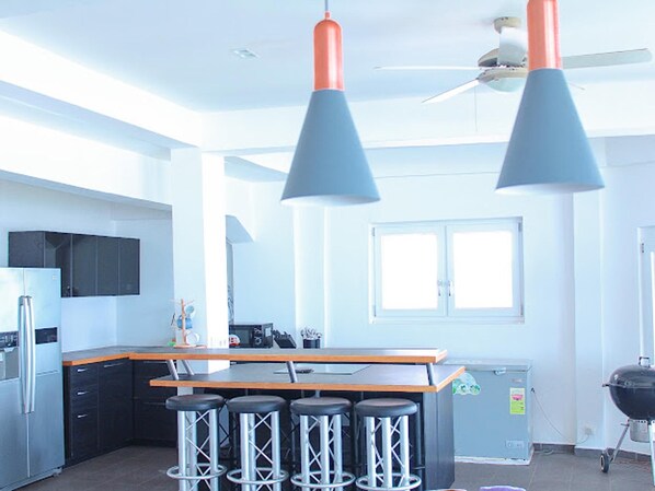 A modern kitchen with a bar area, stainless steel appliances, and a ceiling fan. - Impeccable 3-bed House in Prampram Accra (Prampram)