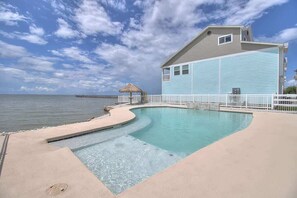 A pool with a curved edge, a building with a light blue exterior, and a pier extending into the water.