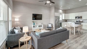 Ein modernes Wohnzimmer mit grauem Sofa, einem kleinen runden Tisch und einem Deckenventilator.