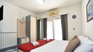 A hotel room with a bed, a wardrobe, a radiator, and a clock on the wall.