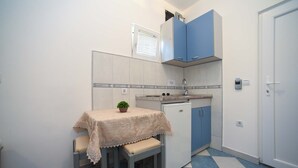 A compact kitchen with a table, stools, a small refrigerator, and blue cabinets.