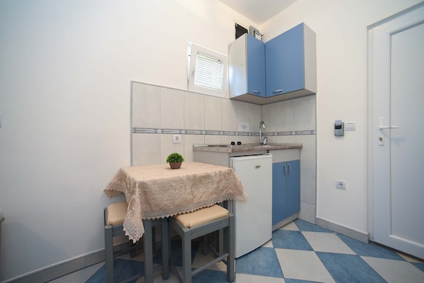 A compact kitchen with a table, stools, a small refrigerator, and blue cabinets.