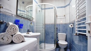 A modern bathroom with a glass shower enclosure, a toilet, and a sink with a towel stack.