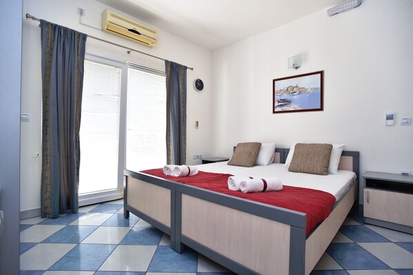 Une chambre d’hôtel avec un lit, une table de chevet, une commode, une horloge murale, un tableau et une fenêtre avec des rideaux.