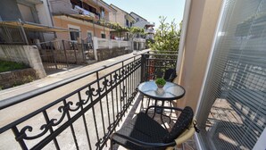 A balcony with a table and two chairs, a small potted plant, and a view of neighboring buildings.