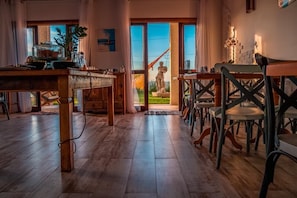 A cozy restaurant with wooden flooring, a central table with chairs, and a statue in the background. - Mar Egeu Arte & Pouso (Peruíbe)