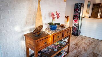 A wooden sideboard with a blue vase and pink orchids, a sailboat model, and magazines on a shelf.