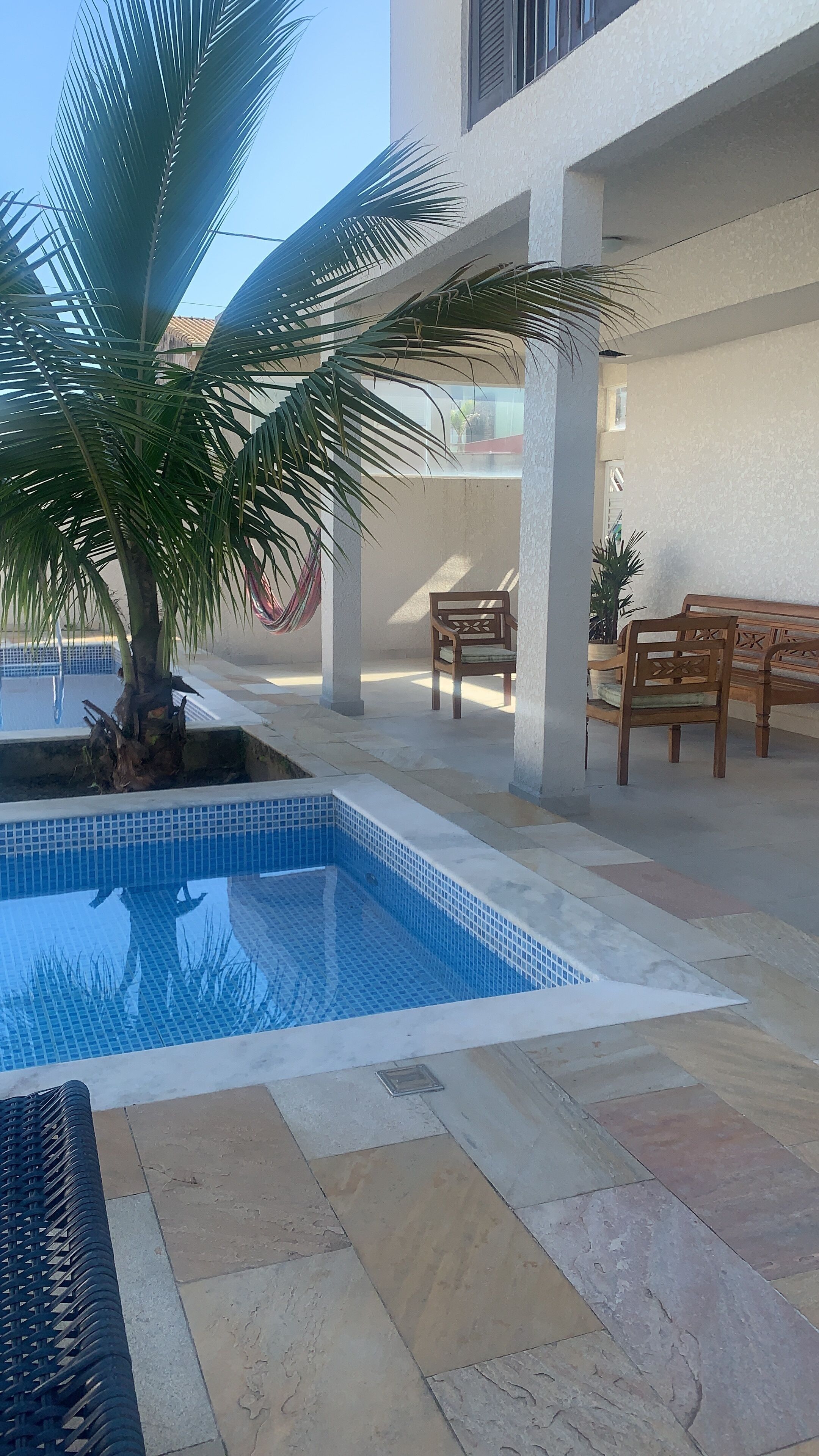A swimming pool with tiled edges, surrounded by stone tiles and a palm tree.