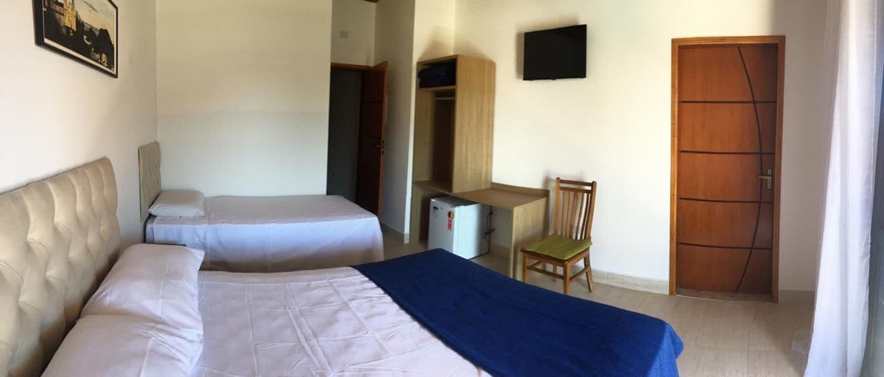 Habitación de hotel con dos camas, un escritorio, una silla, un armario y un televisor.