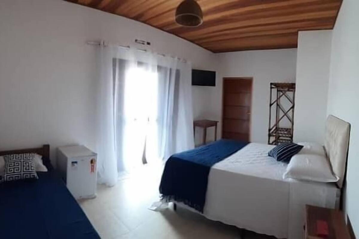 A bedroom with two beds, a wooden ceiling, a small bedside table, and a window with curtains.