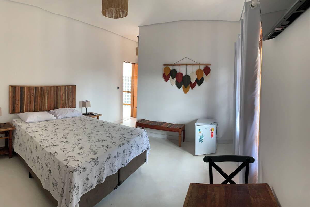 A bedroom with a bed, bedside tables, a desk, a chair, a refrigerator, and a wall-mounted decoration.