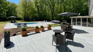 Une terrasse en bois avec des meubles d’extérieur, une piscine et un espace salon abrité.