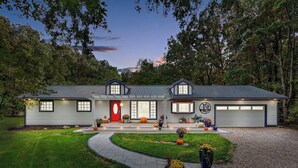 Une maison à deux étages avec un garage, une porte rouge et une allée menant à l’entrée.