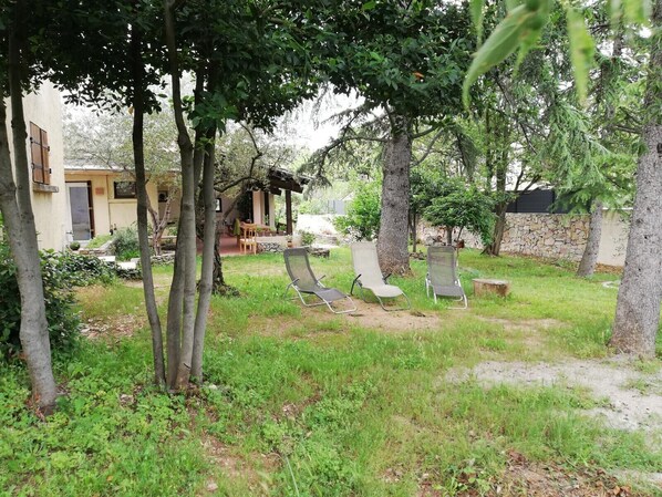 An outdoor seating area with two lounge chairs, a stone wall, and a building with a door and windows in the background.
