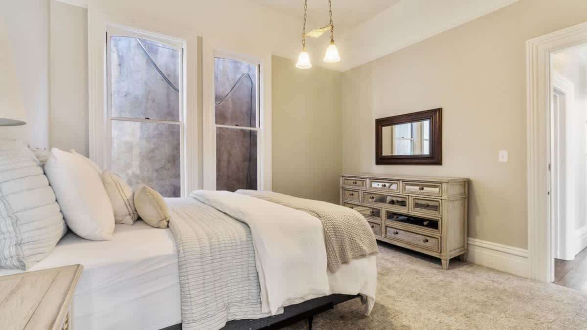 Un dormitorio con cama, cómoda y dos ventanas.