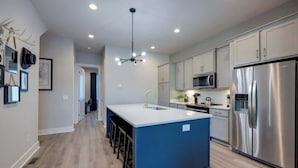 Une cuisine moderne dotée d’un îlot central, d’appareils électroménagers en acier inoxydable et d’un luminaire suspendu.