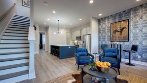 Un salon moderne avec un escalier, une cuisine en arrière-plan et un mur orné d’un motif bleu.