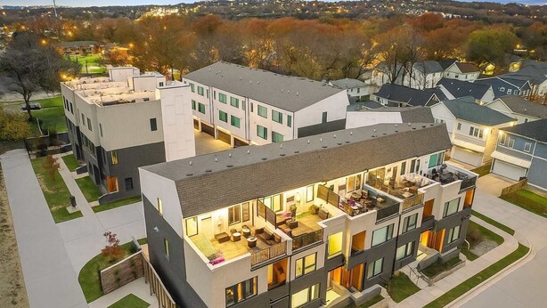 Un immeuble résidentiel moderne à plusieurs étages, doté d’un patio sur le toit, de grandes fenêtres et d’une pelouse bien entretenue.