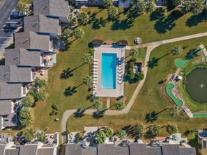 An aerial view of a residential area with a swimming pool, green lawns, and palm trees.