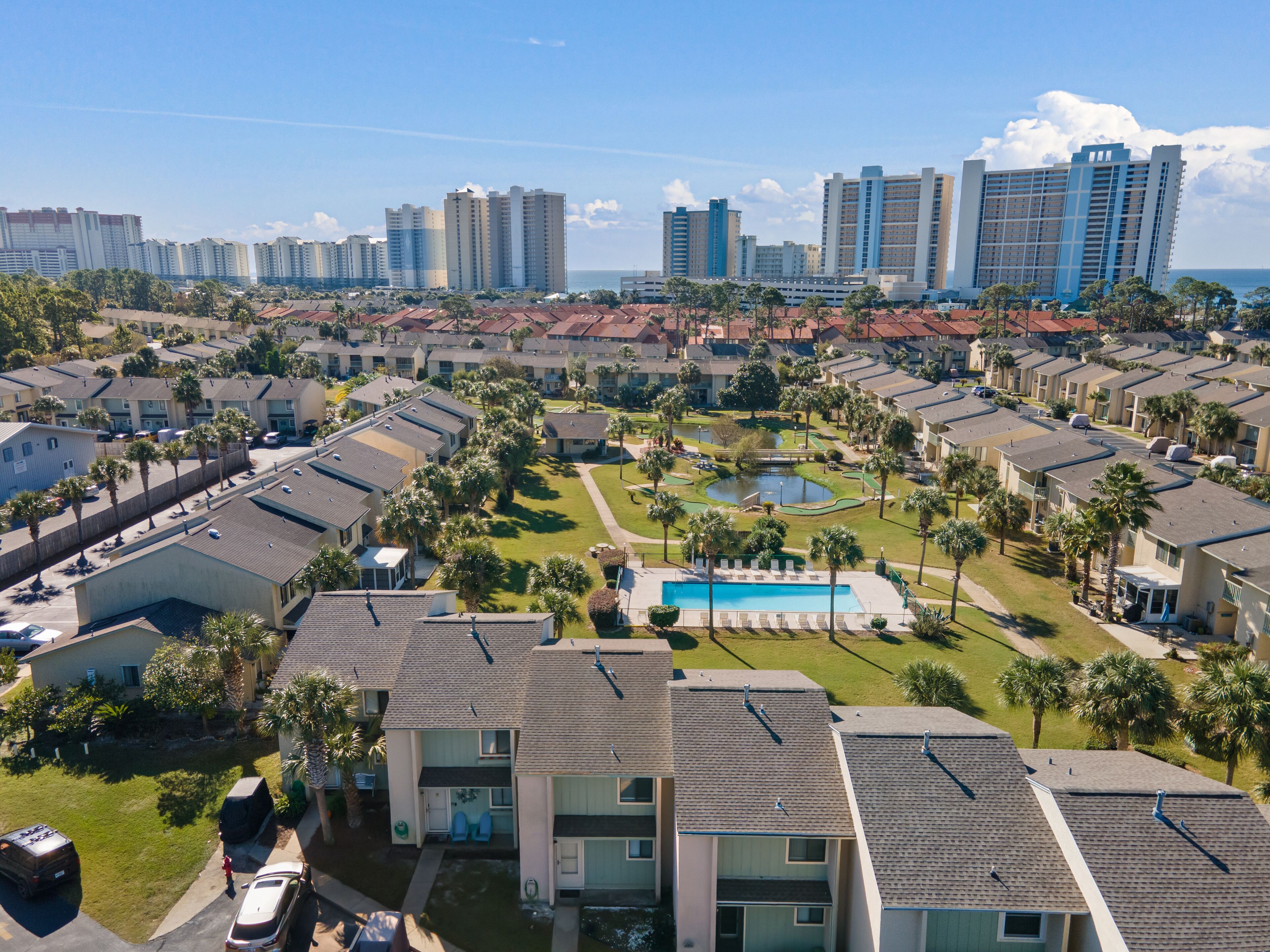 A residential area with modern apartment buildings, a swimming pool, and a small park with palm trees.