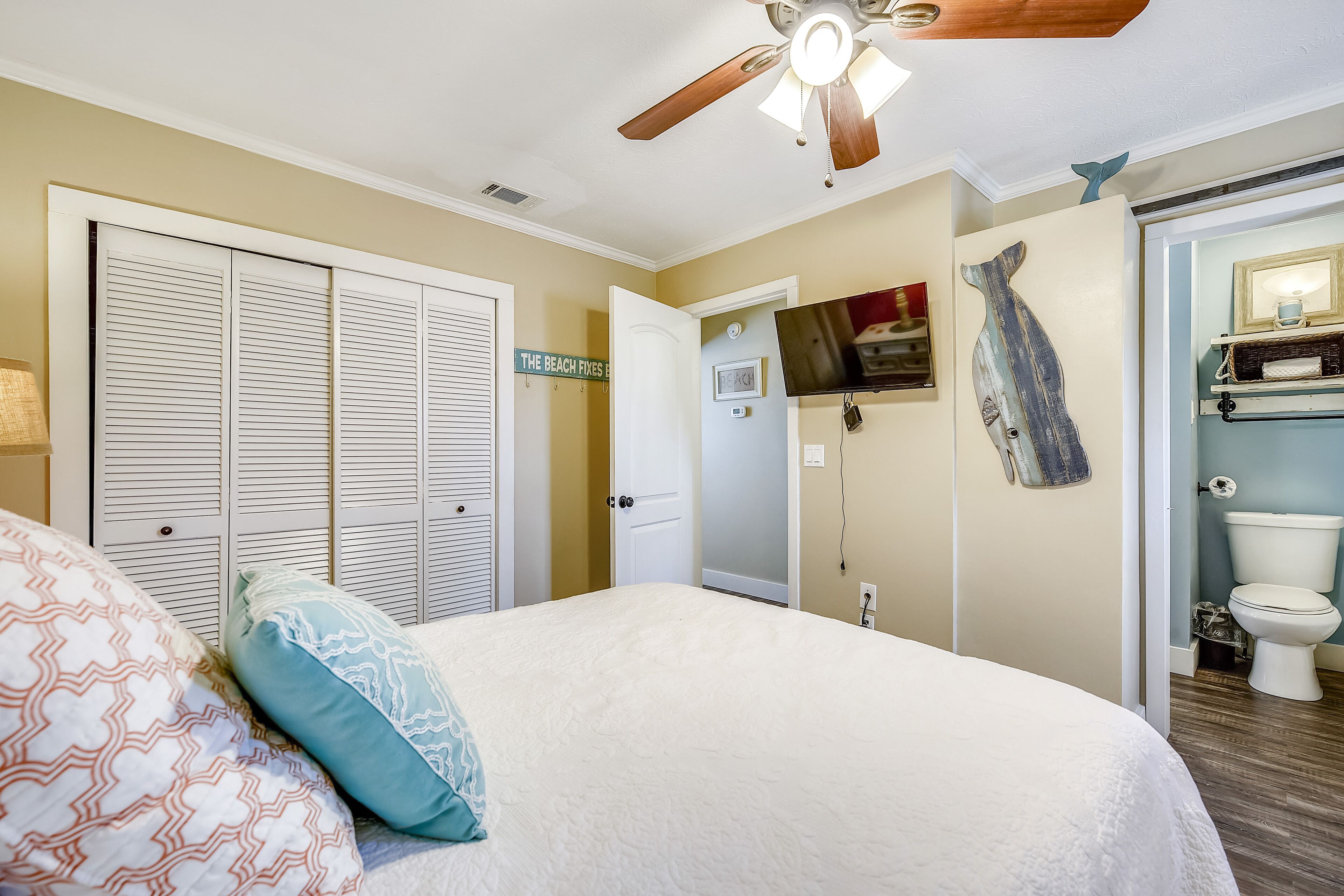A bedroom with a bed, a ceiling fan, a closet, a bathroom with a toilet, and a sign on the wall.