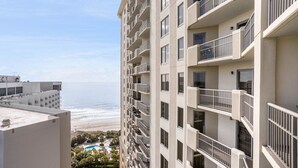Hotel alto com várias varandas dando vista para uma praia e uma área de piscina.