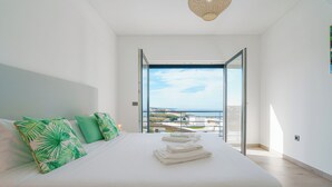 A bedroom with a large bed, green pillows, and a view of the sea through an open door. - Silver Villa with ocean view (Atalaia)