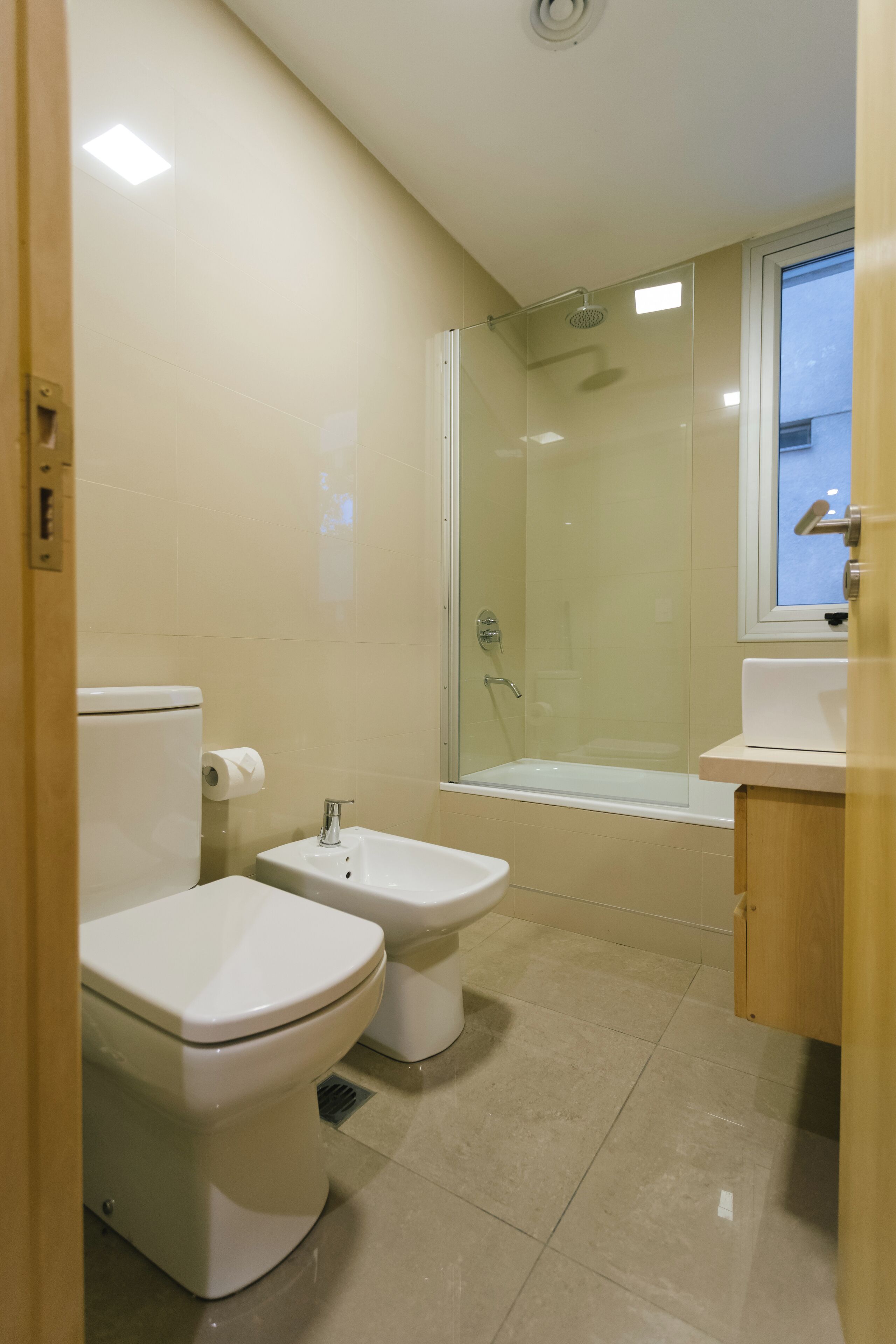 Un baño moderno con inodoro, bidé, bañera y ducha con mampara de vidrio.
