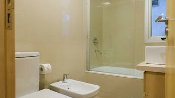 Un baño moderno con inodoro, bidé, bañera y ducha con mampara de vidrio.