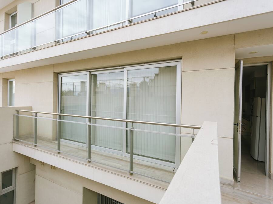 A modern building with a balcony, large windows, and a door leading to an interior space.