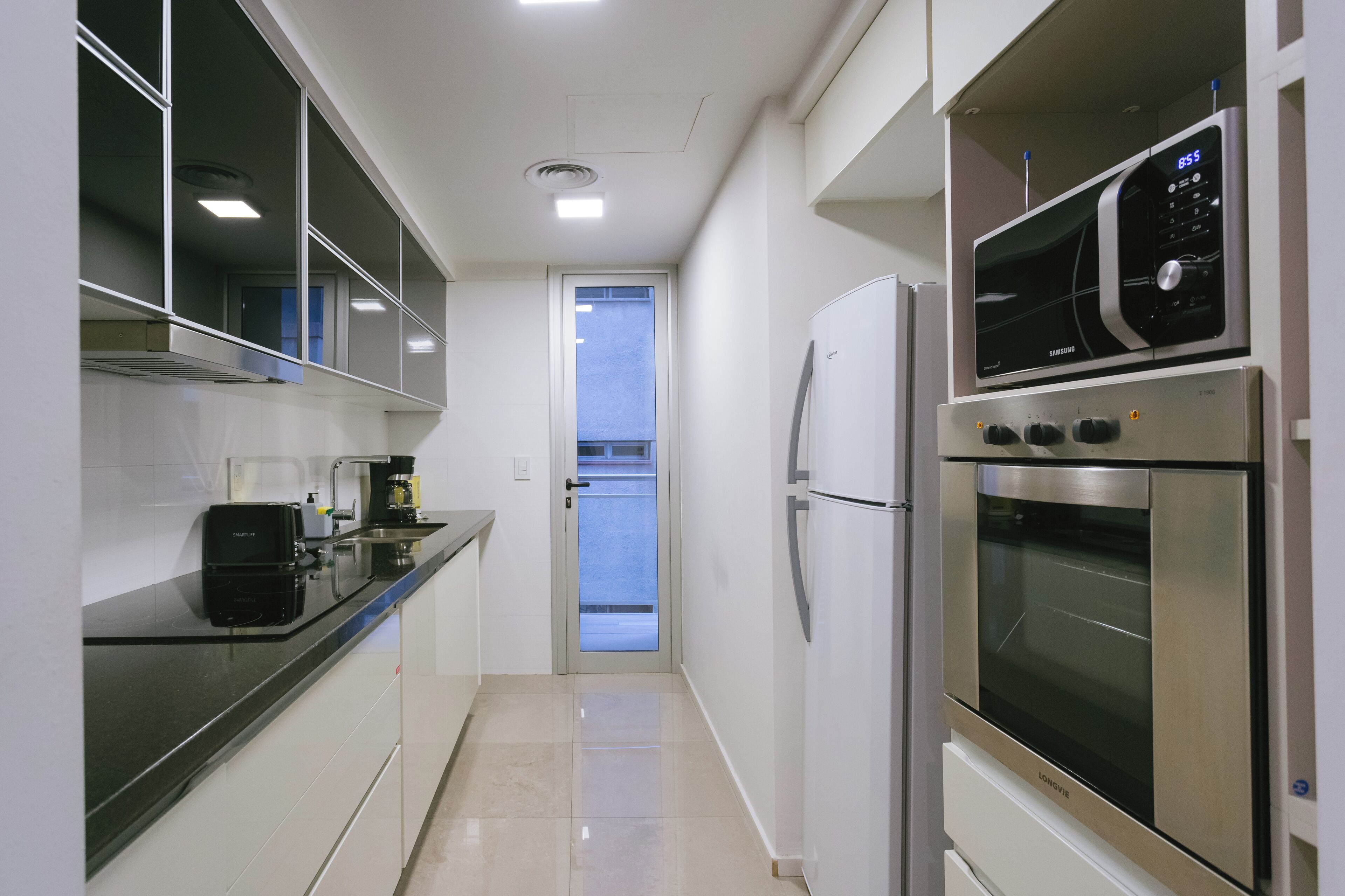 A modern kitchen with a black countertop, stainless steel appliances, and a view to the outside.