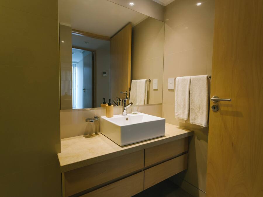 Un baño moderno con un espejo grande, un lavabo blanco y muebles de madera.