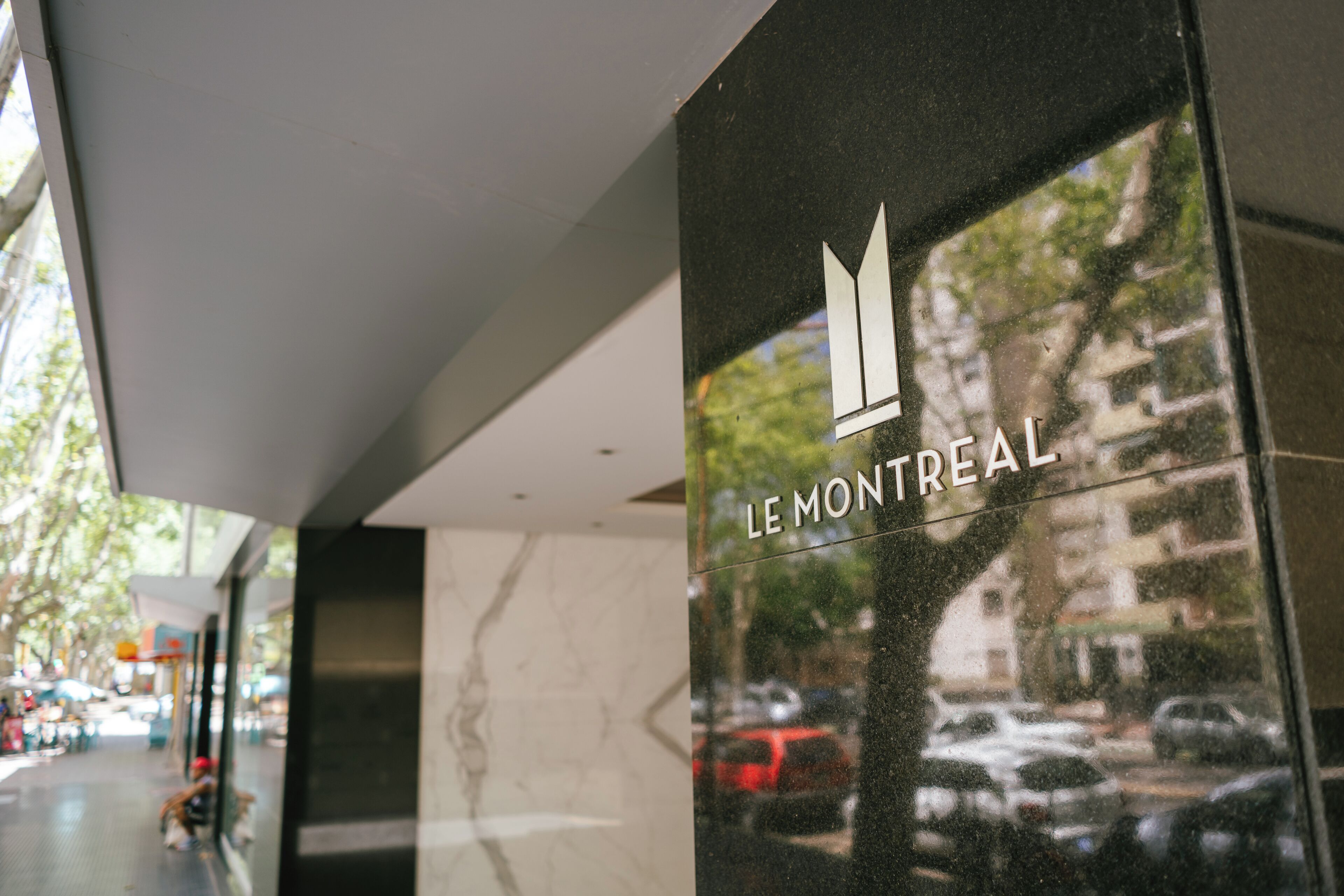 A modern building facade with a glass window reflecting a street scene, including parked cars and trees.