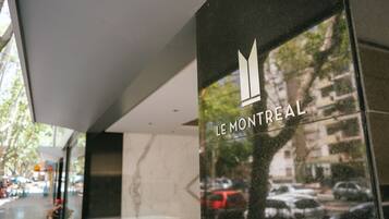 A modern building facade with a glass window reflecting a street scene, including parked cars and trees.