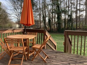 Una terraza de madera con una mesa, sillas y un paraguas naranja, además de una barandilla de madera.