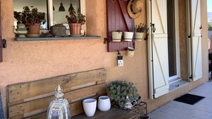 Fachada de un edificio rústico con plantas en macetas en el alféizar, un banco de madera y un portón de metal.