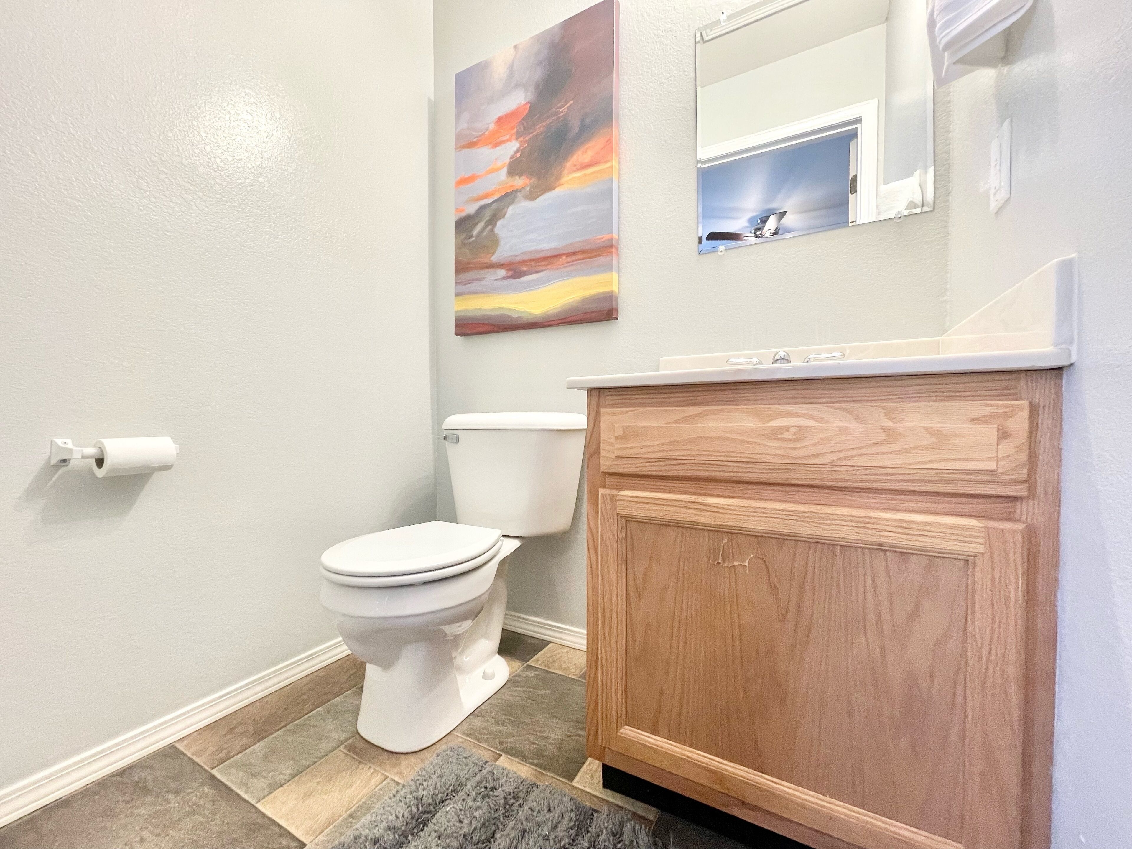 A bathroom with a toilet, wooden vanity, and a painting on the wall.