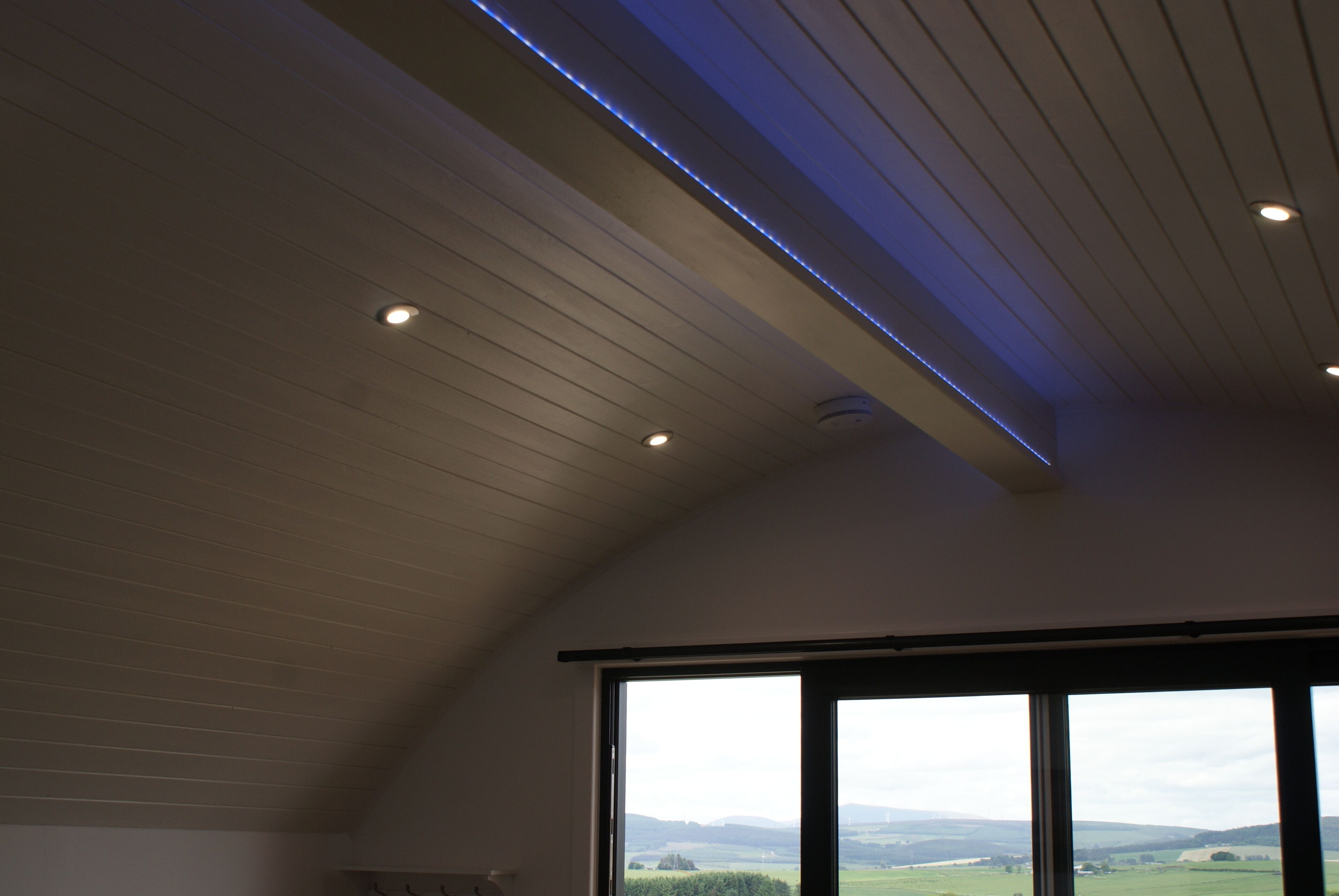 A room with a sloped ceiling, recessed lighting, and a large window offering a view of the countryside.