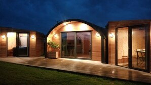 A modern wooden cabin with a glass door entrance, a small outdoor seating area, and a potted plant. - Hillhead Hideaways (Keith)