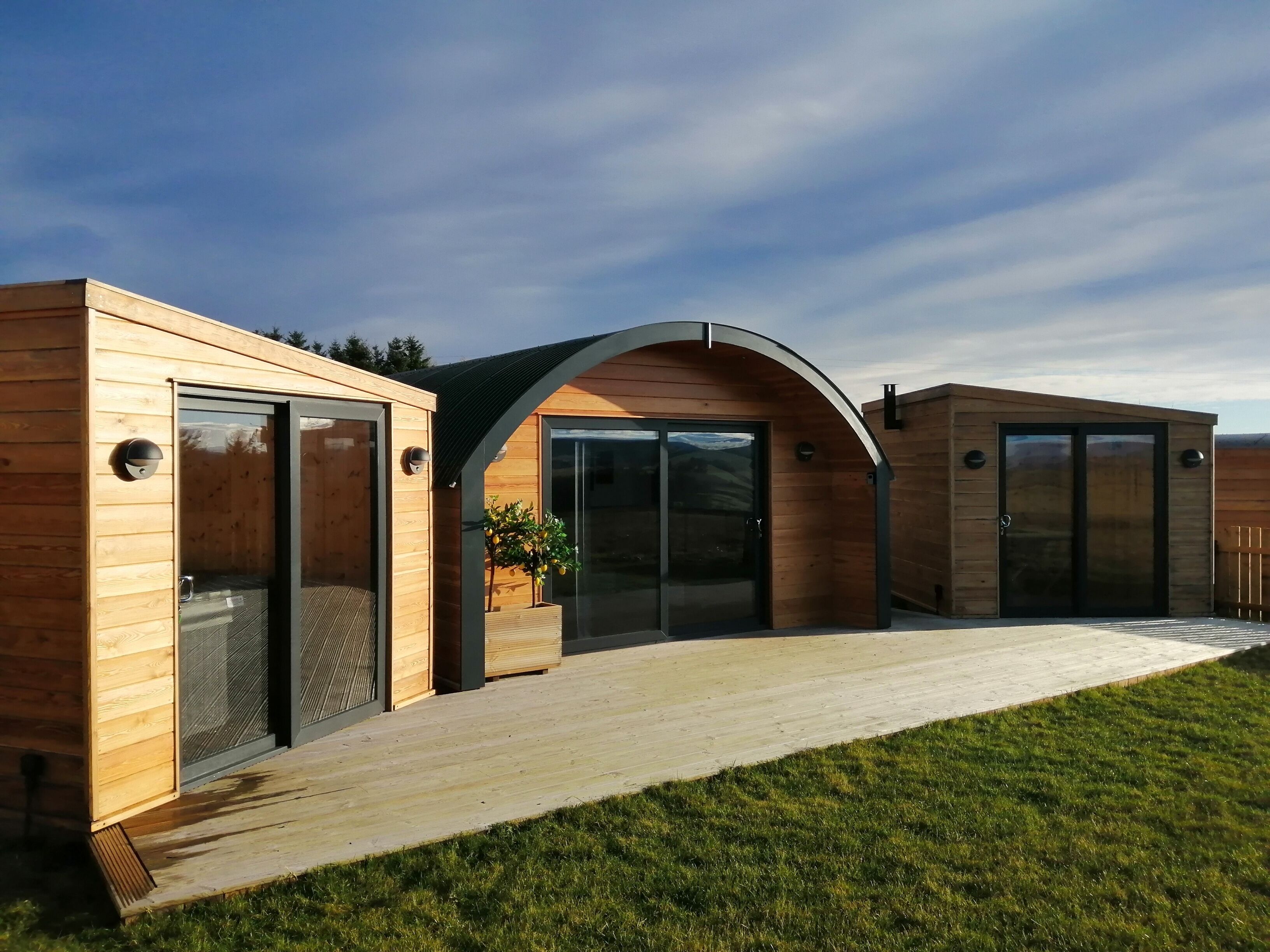 A modern wooden cabin with large sliding glass doors, a covered patio, and a small garden area.