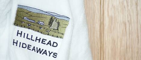 A white garment with embroidered text "HILLHEAD HIDEAWAYS" and a landscape illustration.