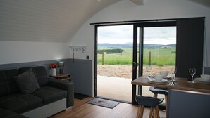 A modern kitchen with a dining area, a sofa, and a view of the countryside. - Hillhead Hideaways (Keith)